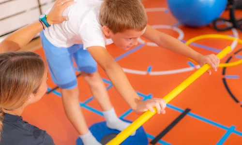 boy-using-balance-board-with-trainer-s-assistance-2026-03-10-02-09-49-utc